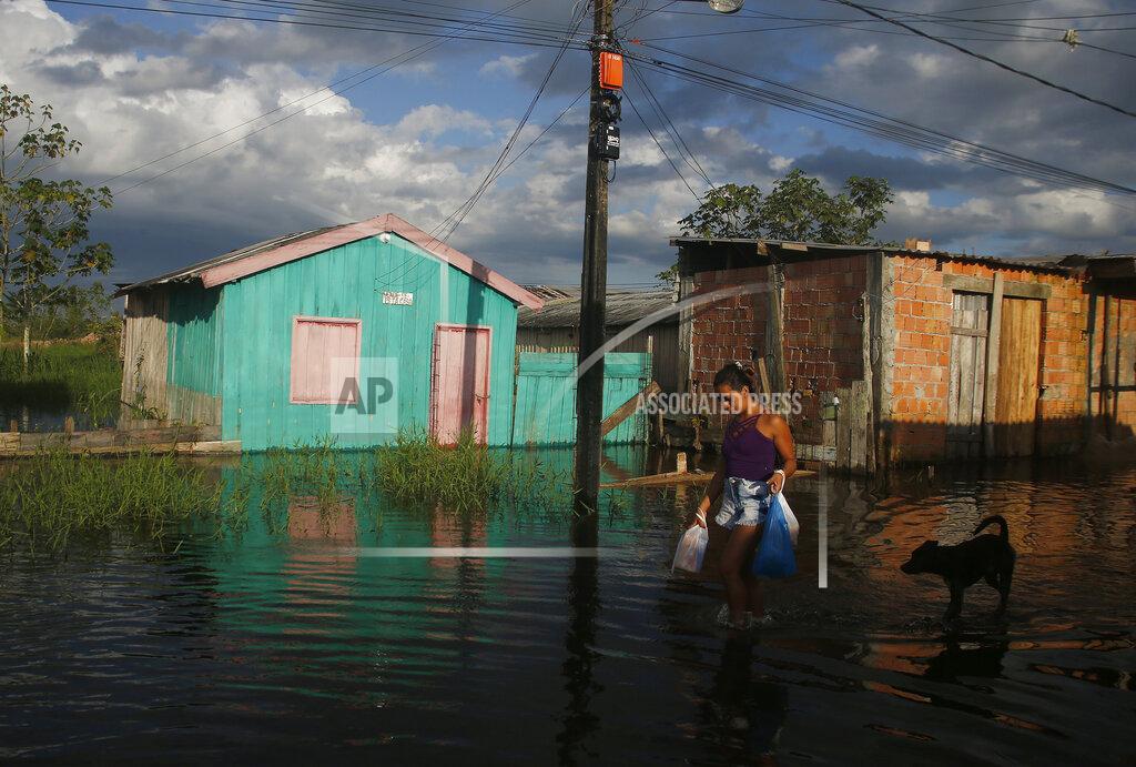 Edmar Barros A woman walks on a street flooded by the rise of the Negro river in Iranduba, Amazonas state, Brazil, Monday, May 23, 2022. The Amazon region is being hit hard by flooding with 35 municipalities that are facing one of their worst floods in years and the water level is expected to rise over the coming months. (AP Photo/Edmar Barros)