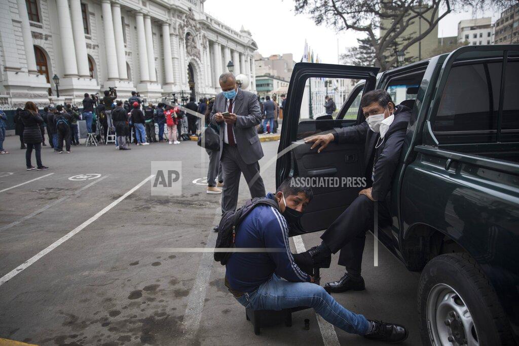 Rodrigo Abd A shoe shiner works on a police officer's shoes during his break from providing security to Congress in Lima, Peru, Friday, Sept. 18, 2020. Peruvian President Martin Vizcarra’s job is on the line Friday as opposition lawmakers push through an impeachment hearing criticized as a hasty and poorly timed ouster attempt in one of the countries hardest hit by the coronavirus pandemic. (AP Photo/Rodrigo Abd)