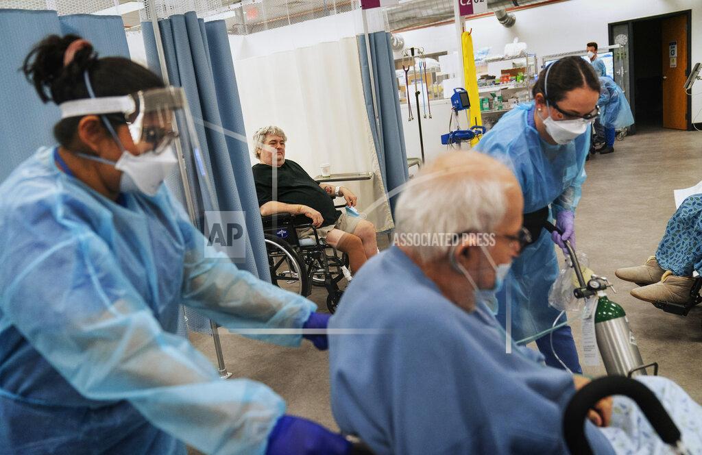 David Goldman COVID-19 patient Art Singleton, 56, rear, watches as fellow patient Nicholas DiPompo, 78, is wheeled to the exit by registered nurses, Doris McClellan, left, and Ashley Nowlin, right, for discharge from a field hospital in Cranston, R.I, Wednesday, Jan. 6, 2021. DiPompo was finally going home. "You got my number," DiPompo shouted to Singleton, whom he'd grown close to after three weeks together. "Give me a call when you get out." He said they would go to his favorite restaurant for baked stuffed lobster. (AP Photo/David Goldman)