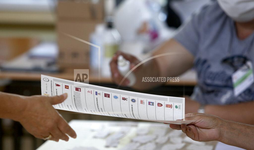 Boris Grdanoski A member of the electoral committee right, gives a ballot to a woman, in a polling station in Skopje, North Macedonia, Wednesday, July 15, 2020. Voters in North Macedonia headed to the polls on Wednesday in the country's general election despite an alarming spike in coronavirus cases in the tiny Balkan nation. (AP Photo/Boris Grdanoski)