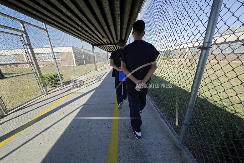 FILE - In a Thursday, Sept. 26, 2019 file photo, detainees walk with their hands clasped behind their backs along a line painted on a walkway inside the Winn Correctional Center in Winnfield, La. Asylum seekers detained at an immigration jail in northern Louisiana are refusing to move into their cells in what their families say is a protest of their prolonged detention. U.S. Immigration and Customs Enforcement confirmed Tuesday, Dec. 2 that there is an ongoing protest at the Winn Correctional Center in rural Winnfield. (AP Photo/Gerald Herbert, File)