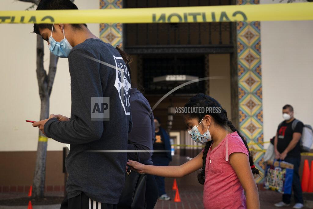 Jae C. Hong FILE - In this Dec. 9, 2020 file photo Hailey Campos, right, grabs her mother's handbag while waiting in line for a COVID-19 test at a testing site in Los Angeles. California became the first state to record 2 million confirmed coronavirus cases, reaching the milestone on Christmas Eve as close to the entire state was under a strict stay-at-home order and hospitals were flooded with the largest crush of cases since the pandemic began. (AP Photo/Jae C. Hong,File)