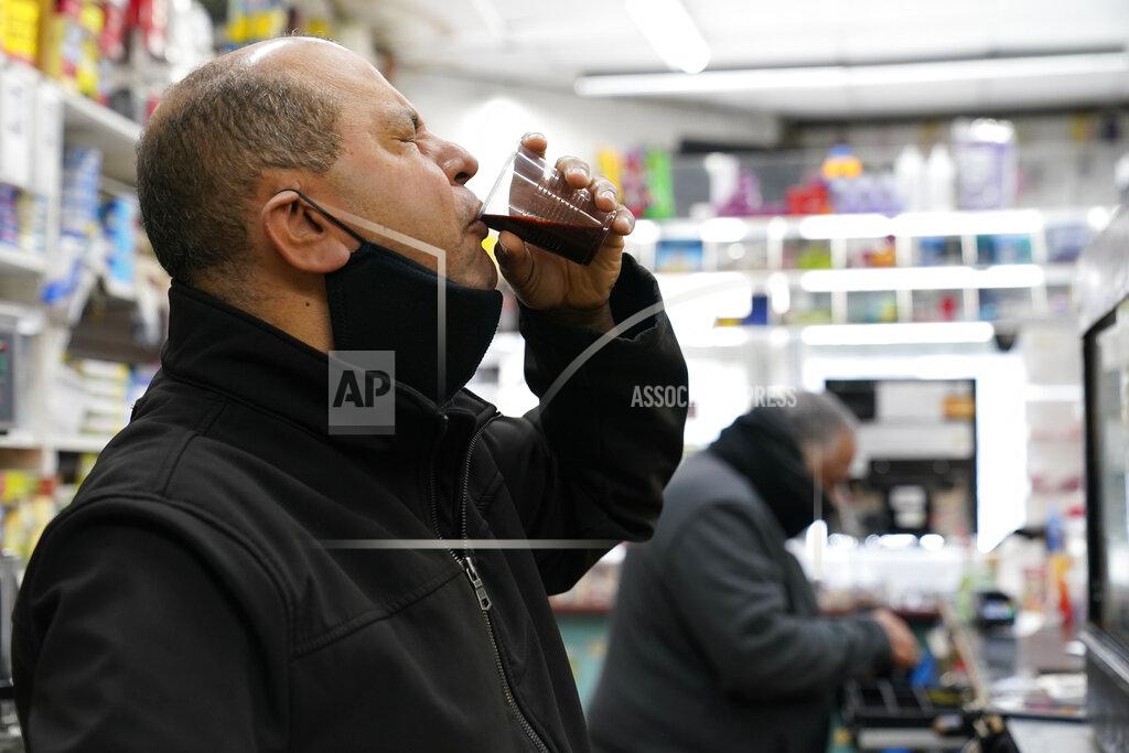 Kathy Willens Bronx bodega owner Francisco Marte winces as he sips a homemade concoction containing garlic, carrots, beets, onion and ginger and other ingredients that he hopes will improve his immune system while he waits for the opportunity to get a COVID-19 vaccination, Wednesday, Feb. 10, 2021, at his store in the Bronx borough of New York. Marte, who heads up the Bodega and Small Business Group, which represents bodegas in New York, lobbied local officials to set aside vaccine appointments for bodega workers, many of whom are unaware they are eligible. He hopes the recent opening of a large vaccination site at Yankee stadium will make access easier for people like him. (AP Photo/Kathy Willens)