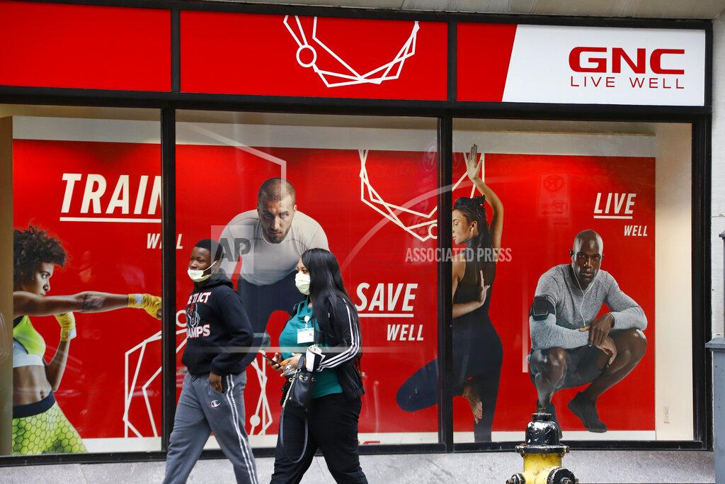 Gene J. Puskar FILE- In this April 29, 2020 file photo, a couple walks past a GNC store at the company's world headquarters in downtown Pittsburgh. The outbreak of the coronavirus has dealt a shock to the global economy with unprecedented speed. Health and wellness company GNC Holdings has filed for Chapter 11 bankruptcy protection and is looking to close at least 800 to 1,200 stores. (AP Photo/Gene J. Puskar, File)