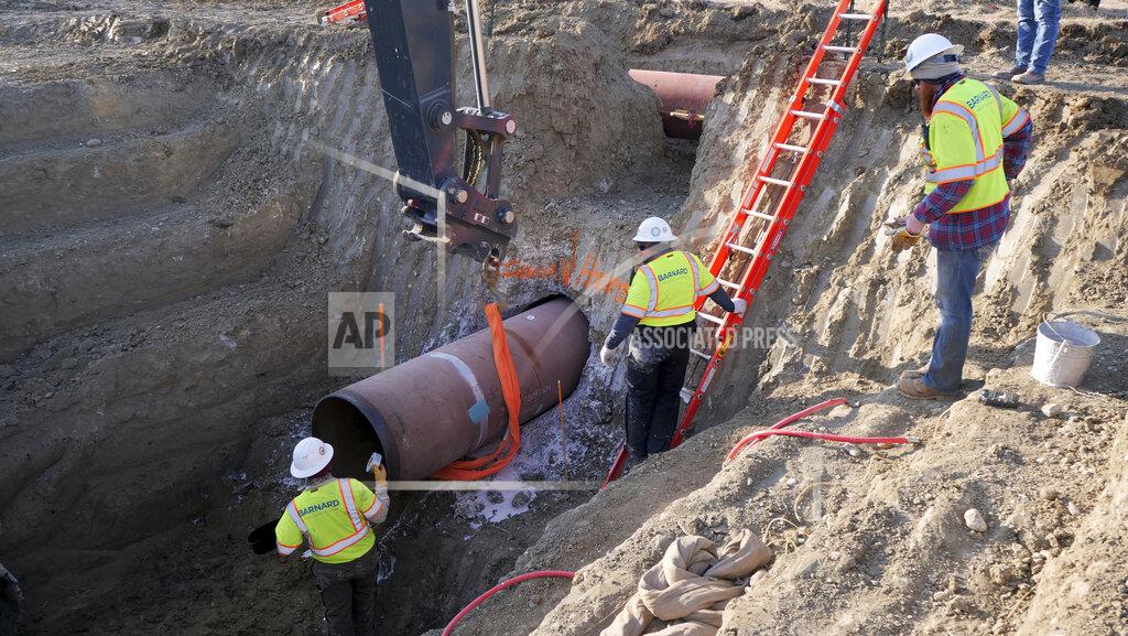 Uncredited This April 13, 2020 photo provided by TC Energy shows workers for TC Energy installing a section of the Keystone XL crude oil pipeline at the U.S.-Canada border north of Glasgow, Mont. Two people working on the Keystone XL oil pipeline have tested positive for the coronavirus in northern Montana, but the company said Thursday, Aug. 8, 2020, that construction work on the disputed project will continue after a temporary shut down of a pipe storage yard. (TC Energy via AP)