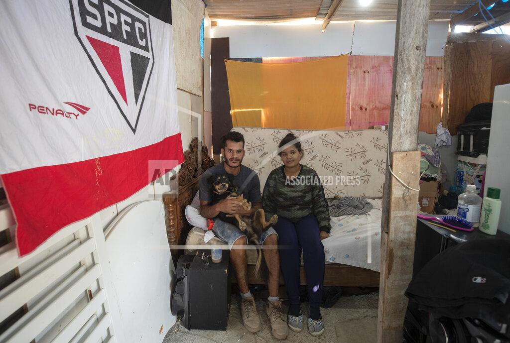 Andre Penner FILE - In this May 15, 2021 file photo, Geovani de Souza, who lost his job as doorman, poses for photos with his wife Juliana Moraes, who is pregnant, inside their home in the Penha Brasil Favela where families have started relocating during the pandemic in Sao Paulo, Brazil. "Without a job, I couldn't pay my rent, was evicted from where I was living and found the solution here," said de Souza, who now relies on occasional work as a bricklayer. (AP Photo/Andre Penner, File)