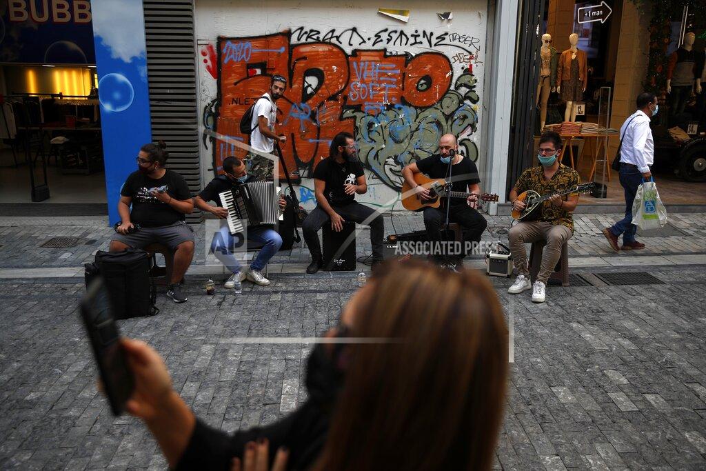 Thanassis Stavrakis Musicians wearing face masks to prevent the spread of the coronavirus, perform as a woman records a video with her cellphone on Ermou Street, Athens' main shopping area, Monday, Oct. 26, 2020. Greece's government has imposed a nightly curfew in greater Athens and other areas with high infection rates as well as more generalized mask use as the daily number of deaths and infections nationwide has rising in recent weeks. (AP Photo/Thanassis Stavrakis)