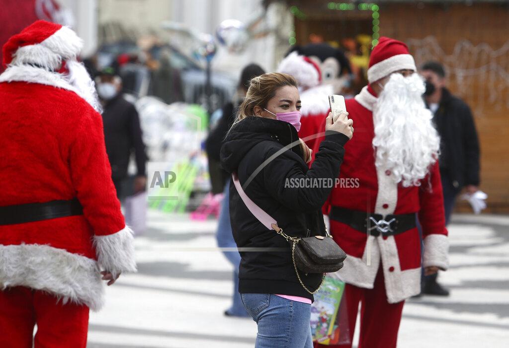 Boris Grdanoski In this picture taken on Tuesday, Dec. 29, 2020, men dressed as Santa Claus hang around, as people wearing face masks walk through downtown Skopje, North Macedonia. When thousands of people across the European Union simultaneously began rolling up their sleeves last month to get a coronavirus vaccination shot, one corner of the continent was left behind, feeling isolated and abandoned: the Balkans. (AP Photo/Boris Grdanoski)