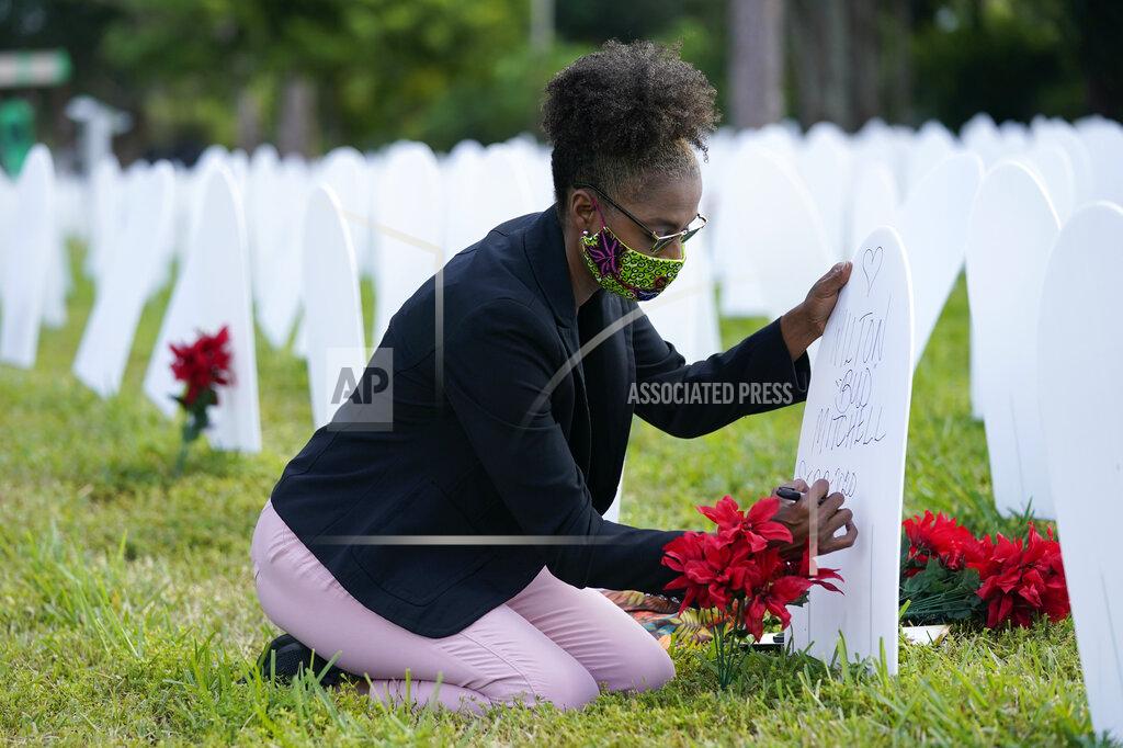 Lynne Sladky Rachel Moore writes a tribute to her cousin Wilton "Bud" Mitchell who died of COVID-19 at a symbolic cemetery created to remember and honor lives lost to COVID-19, Tuesday, Nov. 24, 2020, in the Liberty City neighborhood of Miami. Officials announced that a new COVID-19 testing site will be opening in the neighborhood. (AP Photo/Lynne Sladky)