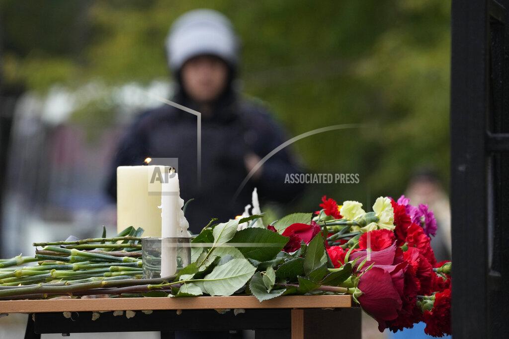 Dmitri Lovetsky Candles and flowers are placed on a table as a police officer stands guard outside the Perm State University following a campus shooting in Perm, about 1,100 kilometers (700 miles) east of Moscow, Russia, Tuesday, Sept. 21, 2021. A student opened fire at the university, leaving a number of people dead and injured, before being shot in a crossfire with police and detained. Beyond saying that he was a student, authorities offered no further information on his identity or a possible motive. (AP Photo/Dmitri Lovetsky)
