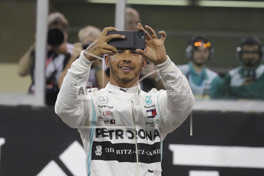 Hassan Ammar Mercedes driver Lewis Hamilton of Britain uses his mobile phone as he celebrates pole position during the qualifying session at the Yas Marina racetrack in Abu Dhabi, United Arab Emirates, Saturday, Nov. 30, 2019. The Emirates Formula One Grand Prix will take place on Sunday. (AP Photo/Hassan Ammar)