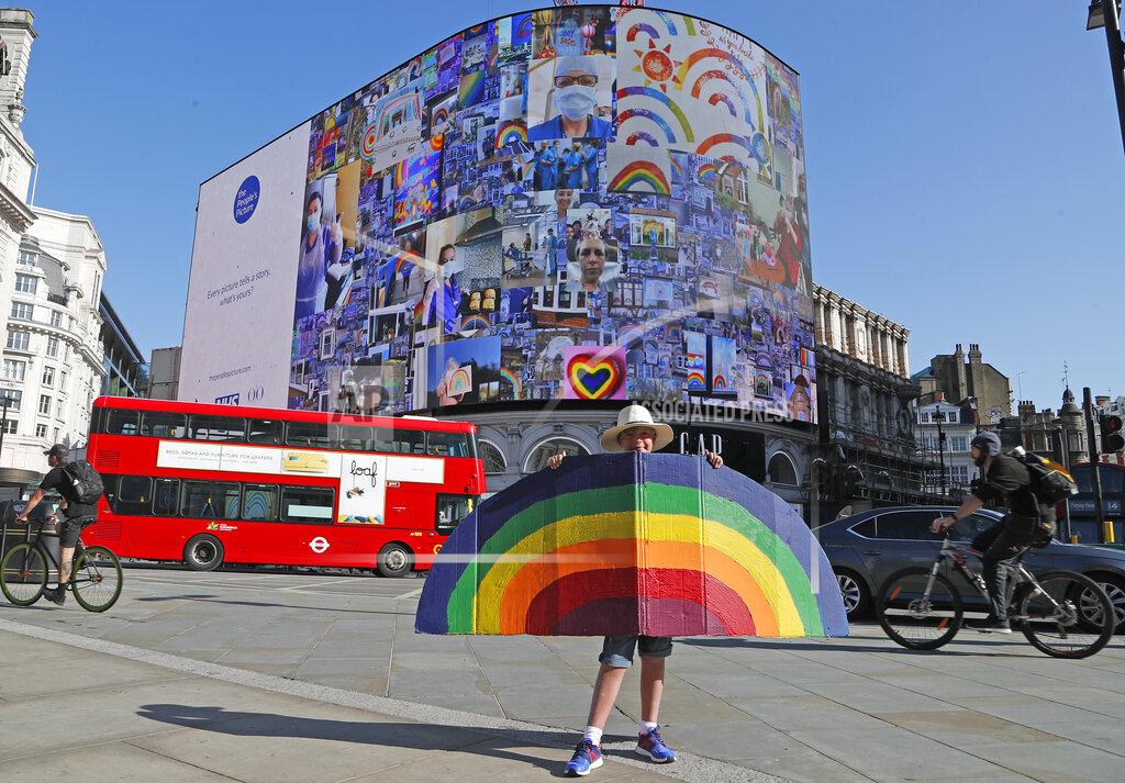 Frank Augstein A young boy holds a painted rainbow as pictures appear on a screen during a 10 minute domination on The Piccadilly Lights, Piccadilly Circus, to mark the launch of The People's Picture interactive mosaic art project Rainbows for the NHS in London, Monday, June 22, 2020. The art installation which features thousands of photos and messages from key workers, carers, patients, doctors and nurses appears on Piccadilly Lights until June 28.(AP Photo/Frank Augstein)