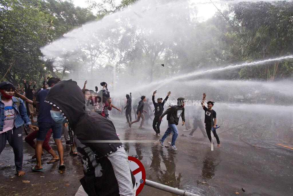 Protesters react as police use a water cannon to disperse them during a rally against a controversial bill on job creation in Medan, North Sumatra, Indonesia, Thursday, Oct. 8, 2020. Thousands of enraged students and workers staged rallies across Indonesia on Thursday in opposition to the new law they say will cripple labor rights and harm the environment. (AP Photo/Binsar Bakkara)