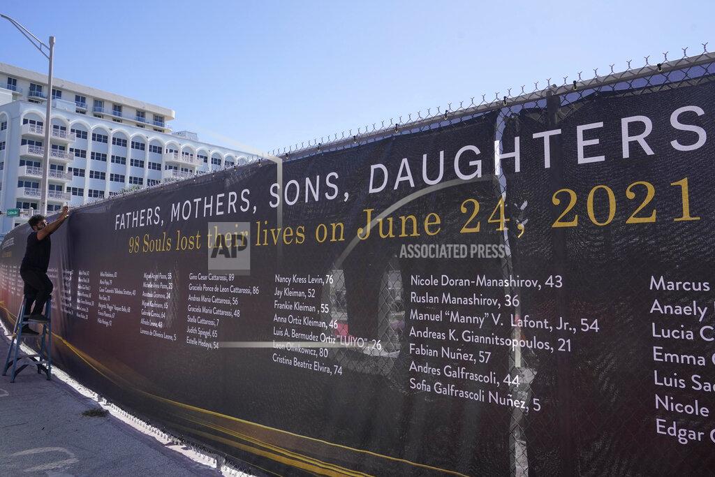 Marta Lavandier Christopher Rosa Cruz installs a large banner at the site of the Champlain Towers South condominium building, Thursday, May 12, 2022, in Surfside, Fla. The banner lists the names of the 98 people killed when the building suddenly collapse nearly a year ago. (AP Photo/Marta Lavandier)