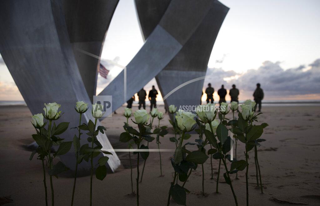Virginia Mayo Men in a vintage US WWII uniforms stand behind flowers left at Les Braves monument after a D-Day 76th anniversary ceremony in Saint Laurent sur Mer, Normandy, France, Saturday, June 6, 2020. Due to coronavirus measures many ceremonies and memorials have been cancelled in the region with the exception of very small gatherings. (AP Photo/Virginia Mayo)