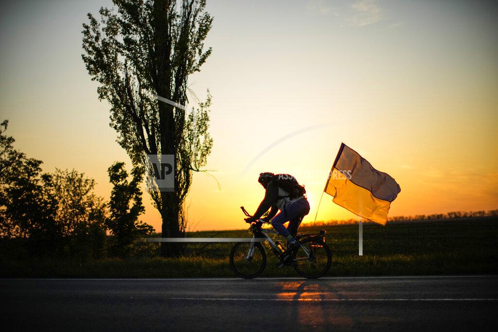Francisco Seco A man rides a bicycle with a Ukrainian flag on the road between Odesa and Mykolaiv, southern Ukraine, Saturday, May 14, 2022. (AP Photo/Francisco Seco)