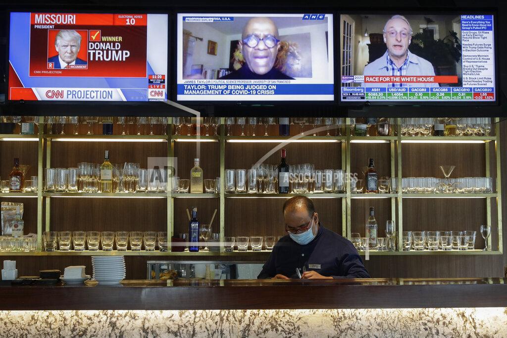 Aaron Favila A waiter works under television sets that show U.S. presidential election reports at a restaurant in Taguig, Philippines, Wednesday, Nov. 4, 2020. (AP Photo/Aaron Favila)