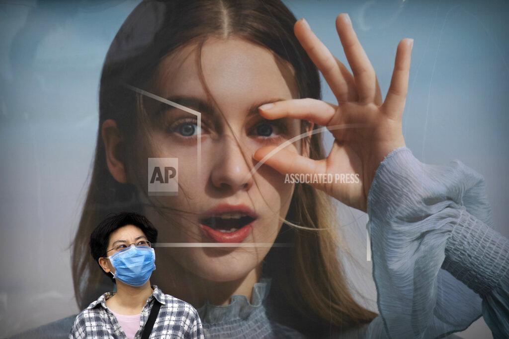 Mark Schiefelbein A woman wearing a face mask to protect against COVID-19 waits in front of a billboard in the central business district in Beijing, Wednesday, May 19, 2021. (AP Photo/Mark Schiefelbein)