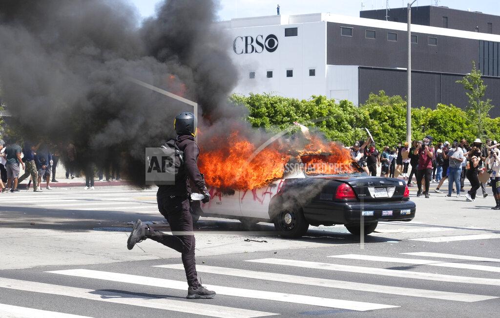 Ringo H.w. Chiu A person runs while a police vehicle is burning during a protest over the death of George Floyd in Los Angeles, Saturday, May 30, 2020. Protests across the country have escalated over the death of George Floyd who died after being restrained by Minneapolis police officers on Memorial Day, May 25. (AP Photo/Ringo H.W. Chiu)