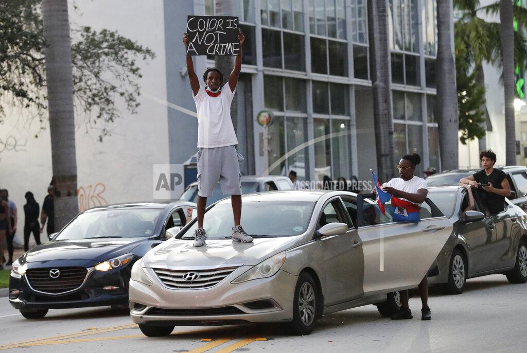 Wilfredo Lee A protester of the death of George Floyd stands on his car as he and others demonstrate Sunday, May 31, 2020, in Miami. Floyd died May 25 after he was pinned at the neck by a Minneapolis police officer. (AP Photo/Wilfredo Lee)