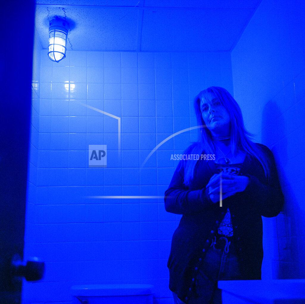David Goldman In this photo made with a medium format film camera, Misti Mann-France stands for a portrait in a bathroom at the laundromat she manages under a blue light installed to make it harder for drug users to find a vein, Thursday, March 18, 2021, in Huntington, W.Va. Hers was among several local businesses to install blue lights at the height of the city's opioid crisis, when they would often find syringes left behind by drug users. "It was the only thing we could think of to do to help," she said. "And it has helped tremendously." She said people have overdosed several times in the parking lot of their business, which includes the laundry and a video poker room. A local gas station chain and liquor store also switched to blue lights. "I wish there was a solution to the bigger problem," she said. "There are so many out there on drugs, and it's sad, it really is." (AP Photo/David Goldman)