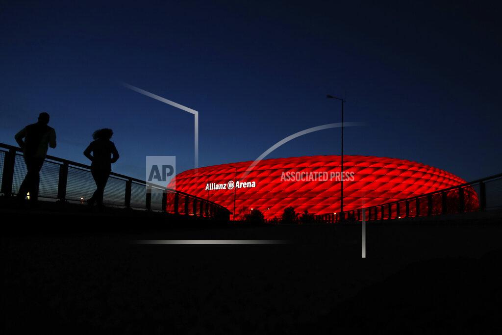 FILE-In this March 16, 2020 taken photo jogger make their way after the sun sets at the 'Allianz Arena' soccer stadium in Munich, Germany. European ruling body UEFA said on Friday the German city of Munich will remain as one of the Euro 2020 host cities. The confirmation came during a UEFA executive board videoconference after the federation was informed by local authorities that all four matches in Munich will be able to welcome a minimum of 14,500 spectators. (AP Photo/Matthias Schrader)