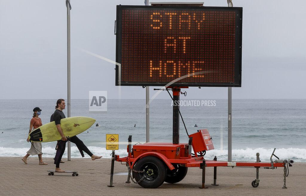 Mark Baker A surfer carries his board as he skates along the beach front at Manly on the northern beaches in Sydney, Australia, Monday, Dec. 21, 2020. Sydney's northern beaches are in a lockdown similar to the one imposed during the start of the COVID-19 pandemic in March as a cluster of cases in the area increased to more than 80. (AP Photo/Mark Baker)