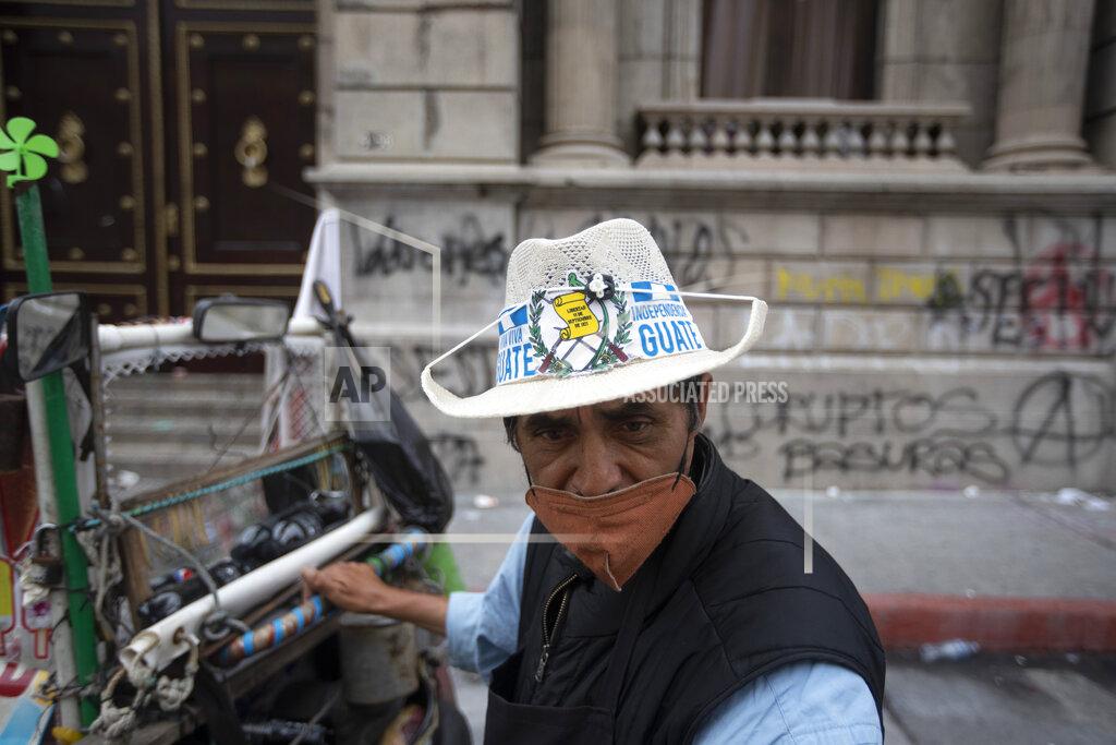 Moises Castillo Ice creme vendor Manuel Sosa walks in front of the Congress building area that was damaged during protests in Guatemala City, Sunday, Nov. 22, 2020. Protesters broke into the building and set it partially on fire amid growing demonstrations against President Alejandro Giammattei and the legislature for approving a controversial budget that cut educational and health spending. (AP Photo/Moises Castillo)