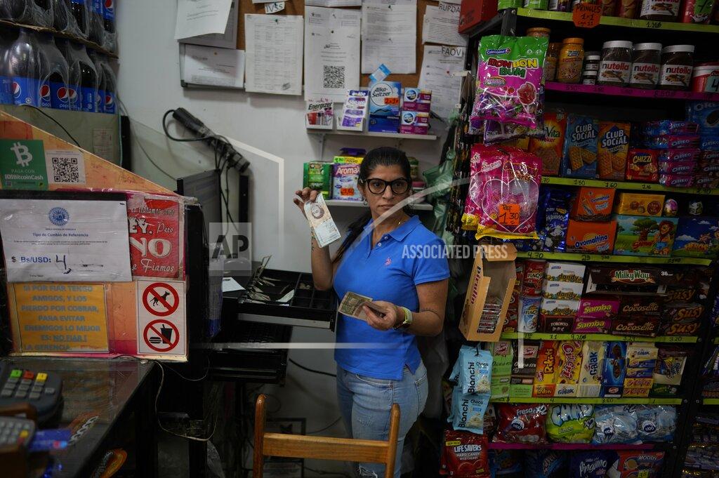 Ariana Cubillos Rim Hassam holds Bolivars and U.S currency that she received from a customer as payment in her shop, in Caracas, Venezuela, Friday, May 13, 2022. A new tax law approved by the Venezuelan government, that went into effect in March, applies a 3% tax charge on transactions paid in foreign currencies. (AP Photo/Ariana Cubillos)