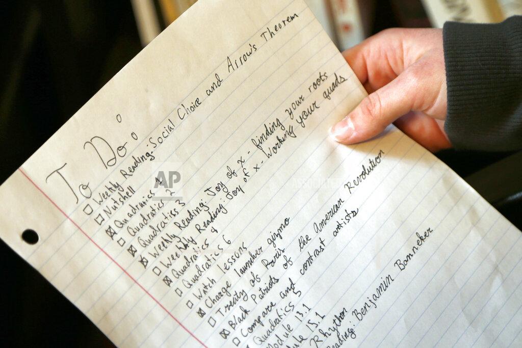 Jay Laprete In this Tuesday, Feb. 23, 2021 photo, Graciela Leahy, 13, an eighth grader at Ohio's Columbus Gifted Academy, holds her school to-do list in her bedroom, in Columbus, Ohio. A year later in the pandemic, the unplanned experiment with distance learning continues for thousands of students like Leahy who have yet to set foot back in classrooms. (AP Photo/Jay LaPrete)