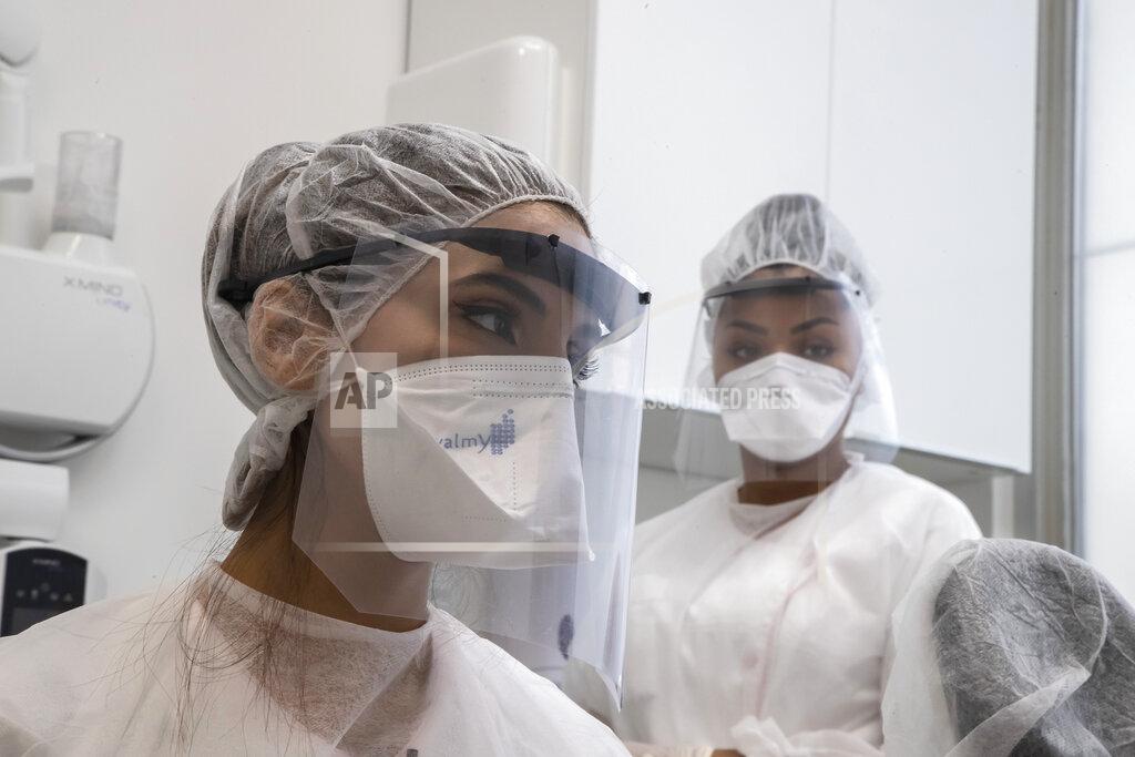 In this Wednesday, May 13, 2020 photo, dentist Sabrine Jendoubi, left, and her assistant Margot Daussat listen to a patient during a dental appointment, at a dental office in Paris. Those with toothache that suffered through France's two-month lockdown, finally have hope to end the pain. Dental practices are cautiously re-opening and non-emergency dentist appointments are now permitted around the country, as the French government eased confinement restrictions from Monday. (AP Photo/Michel Euler)