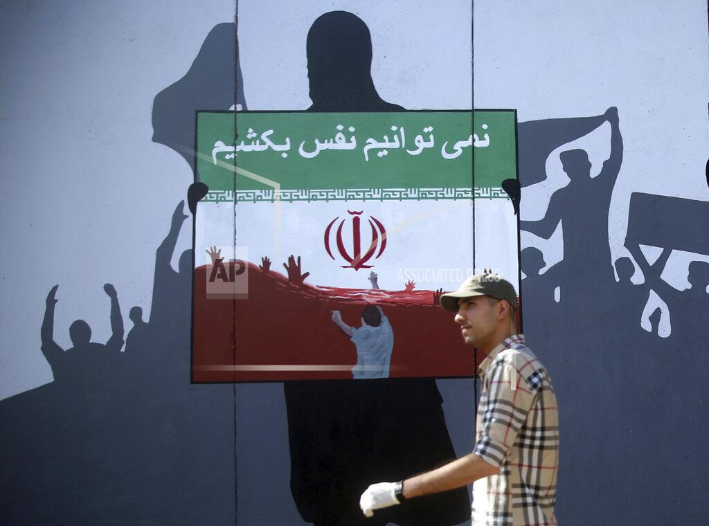 A man walks past a painting on a wall with writing in the Dari Language reading "We cannot breath" during a protest themed Killings of Afghans in Iran in Kabul, Afghanistan, Monday, June 15, 2020. The violent deaths of Afghan refugees inside Iran has sparked an uproar despite denials from Tehran. (AP Photo/ Rahmat Gul)