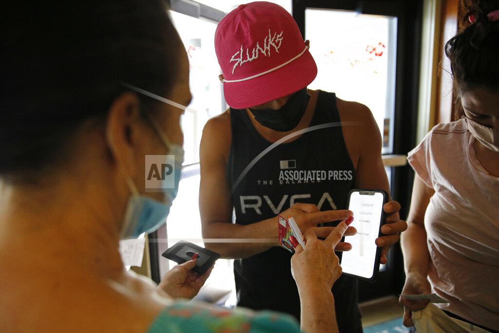 Caleb Jones Highway Inn restaurant hostess Ku'uipo Lorenzo, left, checks a COVID-19 test result from Martin Day, center, as his wife, Ashley Day, right, prepares to show her vaccination card on Monday, Oct. 25, 2021, in Honolulu. To comply with local mandates, the restaurant requires all indoor diners to show proof of vaccination or have a recent negative test result before being seated. (AP Photo/Caleb Jones)
