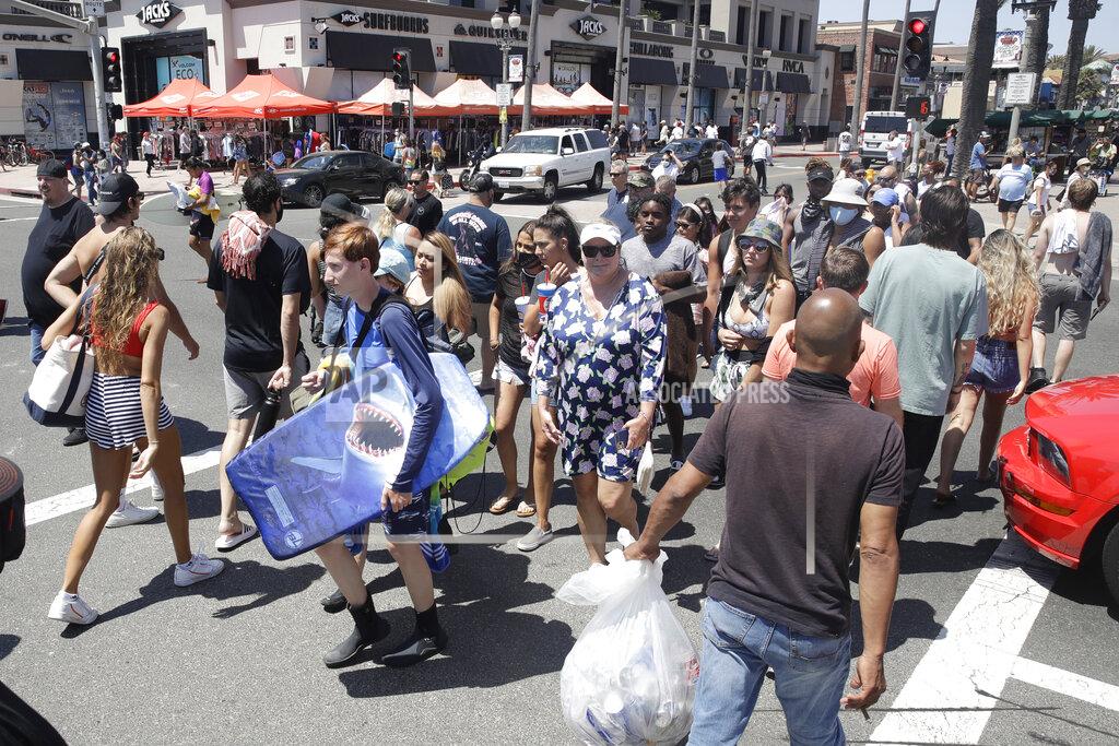 FILE - In this June 27, 2020, file photo, beach goers cross the Pacific Coast Highway in Huntington Beach, Calif. California's mood has gone from optimistic to sour as coronavirus cases and hospitalizations are on the rise heading into the July 4th weekend. Gov. Gavin Newsom has ordered bars and indoor restaurant dining closed in most of the state, many beaches are off limits, and he's imploring Californians to avoid holiday gatherings with family and friends. (AP Photo/Marcio Jose Sanchez, File)