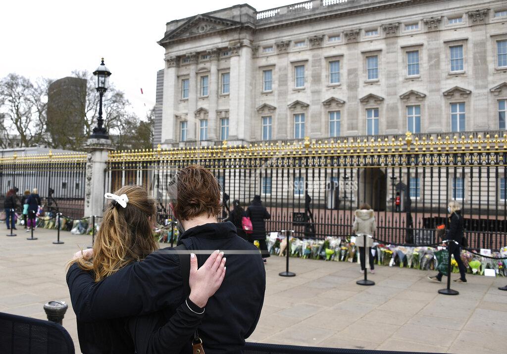 Alberto Pezzali Two people stand behind a barrier as they view flower tributes left in front of the gate at Buckingham Palace in London, a day after the death of Britain's Prince Philip, Saturday, April 10, 2021. Britain's Prince Philip, the irascible and tough-minded husband of Queen Elizabeth II who spent more than seven decades supporting his wife in a role that mostly defined his life, died on Friday. (AP Photo/Alberto Pezzali)