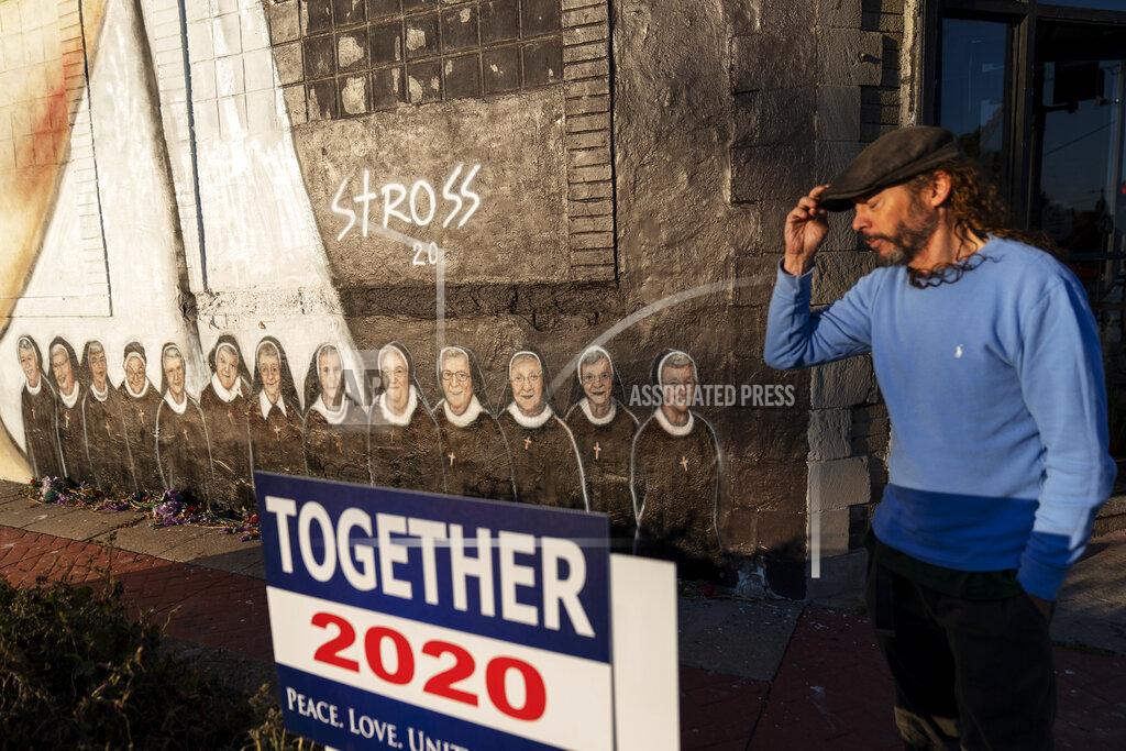 David Goldman Artist Edward Stross stands next the mural he painted to honor the 13 nuns who died at a local convent from COVID-19, at his studio in Roseville, Mich., Saturday, Oct. 31, 2020. As the coronavirus crisis surges to more than nine million infections and 230,000 dead, the election for many is a referendum on how Trump has handled the pandemic. In the final days of the campaign, he has continued to downplay the toll it has taken, and many of his supporters say they find no fault in his response. (AP Photo/David Goldman)