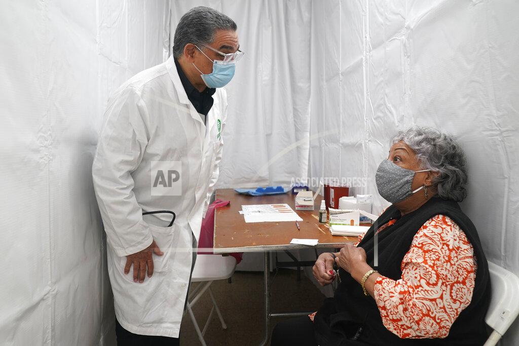 Seth Wenig Dr. Victor Peralta, left, talks with Nellie Hernandez before giving her the second dose of the COVID-19 vaccine in New York, Friday, Feb. 5, 2021. From elderly Cuban Americans in Florida to farmworkers in California, Latinos face daunting barriers like fear, language and a lack of education and access as the COVID-19 vaccines roll out, creating risks for public health as the virus mutates and spreads. (AP Photo/Seth Wenig)