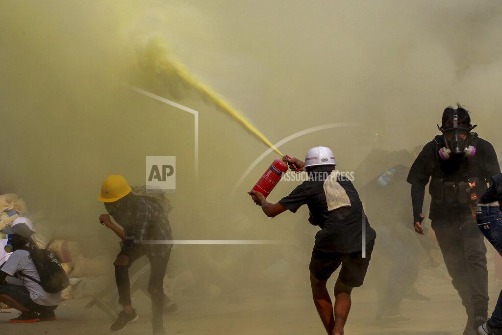 Uncredited FILE - In this March 17, 2021, file photo, an anti-coup protester uses a fire extinguisher to provide cover for others as security forces approach their encampment in Yangon, Myanmar. Garment workers in Myanmar are urging major international brands to denounce the recent military coup there and put more pressure on factories to protect workers from being fired or harassed - or worse arrested and killed for participating in protests. Violent crackdowns by Myanmar security forces against protesters including garment workers are escalating. (AP Photo, File)