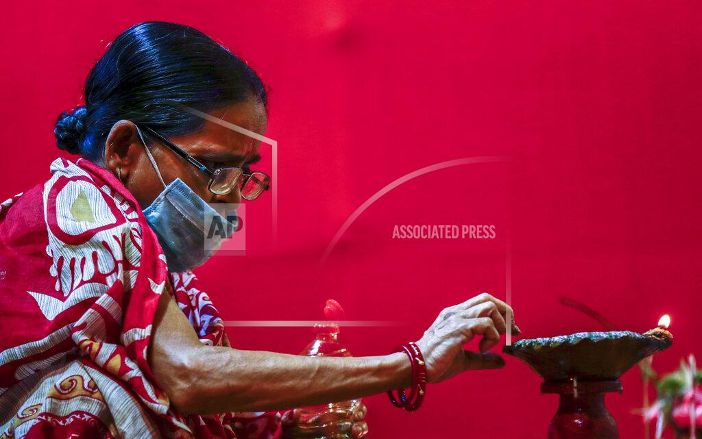 Bikas Das An elderly Indian woman wearing a face mask lights an oil lamp inside a makeshift worship venue during Durga Puja, the biggest festival of the region, in Kolkata, India, Sunday, Oct. 25, 2020. The Hindu festival season is traditionally laced with an unmatched fanfare and extravaganza, with socializing being the hallmark of the celebration. But because of the coronavirus pandemic this year's festivities have started on a pale note. (AP Photo/Bikas Das)