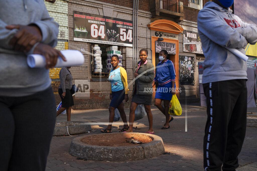 Jerome Delay Three women carrying grocery bags walk past residents lining up to be tested for COVID-19 as well as HIV and Tuberculosis, in downtown Johannesburg Thursday, April 30, 2020. Thousands are being tested in an effort to derail the spread of coronavirus. South Africa will began a phased easing of its strict lockdown measures on May 1, although its confirmed cases of coronavirus continue to increase. (AP Photo/Jerome Delay)