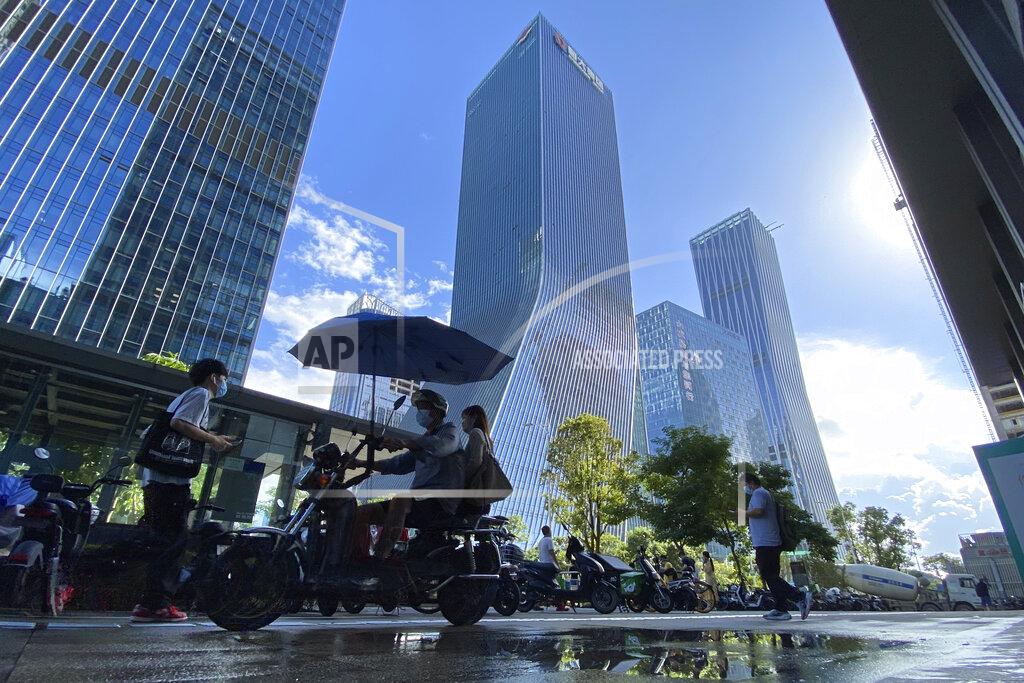 Ng Han Guan Residents pass near the headquarters for Evergrande in Shenzhen in southern China, Thursday, Sept. 23, 2021. The Chinese real estate developer whose struggle to avoid defaulting on billions of dollars of debt has rattled global markets says it will pay interest due Thursday to bondholders in China but gave no sign of plans to pay on a separate bond abroad. (AP Photo/Ng Han Guan)