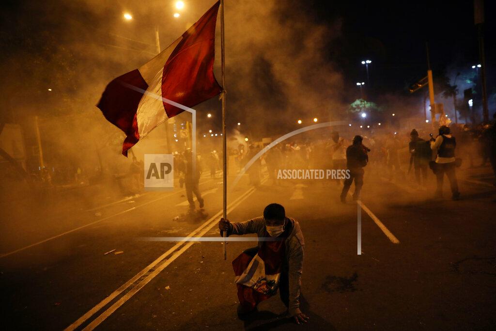 Rodrigo Abd A protester holds a banner with the country's national color as police launch tear gas to disperse protesters who gathered in Plaza San Martin to demonstrate their refusal to recognize Peru's new government, in Lima, Saturday, Nov. 14, 2020. Peru’s Congress voted overwhelmingly to remove now ex-President Martín Vizcarra on Monday. (AP Photo/Rodrigo Abd)