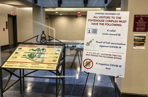 A day after Assembly Republicans successfully defied a mandate to show COVID-19 vaccination proof or a negative test, signs stood around entryways and outside committee rooms at the statehouse showing the mandate remained policy, Friday Dec. 3, 2021, in New York. The New Jersey statehouse requirement for visitors to show proof of COVID-19 or a negative test is still in effect after Republican lawmakers defied it ahead of a voting sessions Thursday. (AP Photo/Mike Catalini)