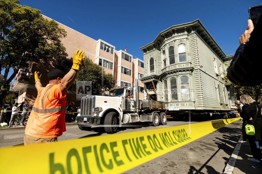 Noah Berger A worker signals to a truck driver pulling a Victorian home through San Francisco on Sunday, Feb. 21, 2021. The house, built in 1882, was moved to a new location about six blocks away to make room for a condominium development. According to the consultant overseeing the project, the move cost approximately $200,000 and involved removing street lights, parking meters, and utility lines. (AP Photo/Noah Berger)