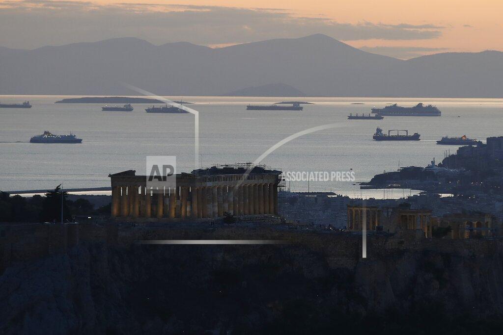 The Parthenon temple is illuminated atop of the Acropolis hill as a ferry approaches the port of Piraeus as another one departs in Athens, Monday, Oct. 26, 2020. (AP Photo/Thanassis Stavrakis)