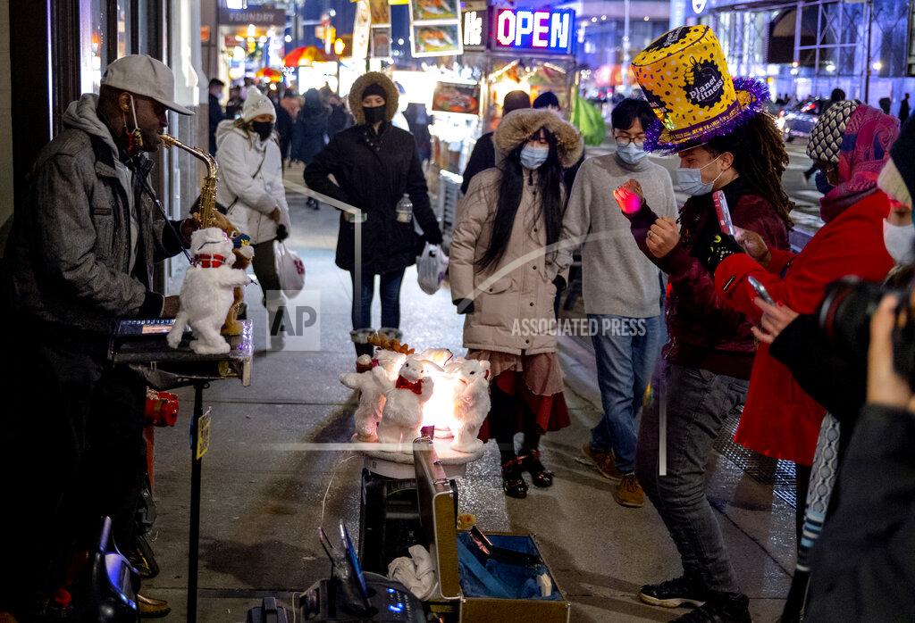 Craig Ruttle Pedestrians pass by and also watch street entertainment on Eighth Avenue, adjacent to a closed-off Times Square in New York, late Thursday, Dec. 31, 2020, as celebrations have been truncated this New Year's Eve due to the ongoing pandemic. (AP Photo/Craig Ruttle)