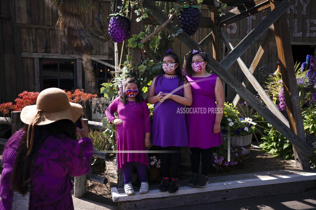 Jae C. Hong Three girls pause for photos with their masks on during the Knott's Taste of Boysenberry Festival at Knott's Berry Farm in Buena Park, Calif., Tuesday, March 30, 2021. Massive Los Angeles County can reopen even more businesses, California public health officials announced Tuesday. The county of 10 million people was one of several counties, including neighboring Orange County, that moved into the state's second-least restrictive orange tier amid low coronavirus case rates and increased vaccinations. (AP Photo/Jae C. Hong)