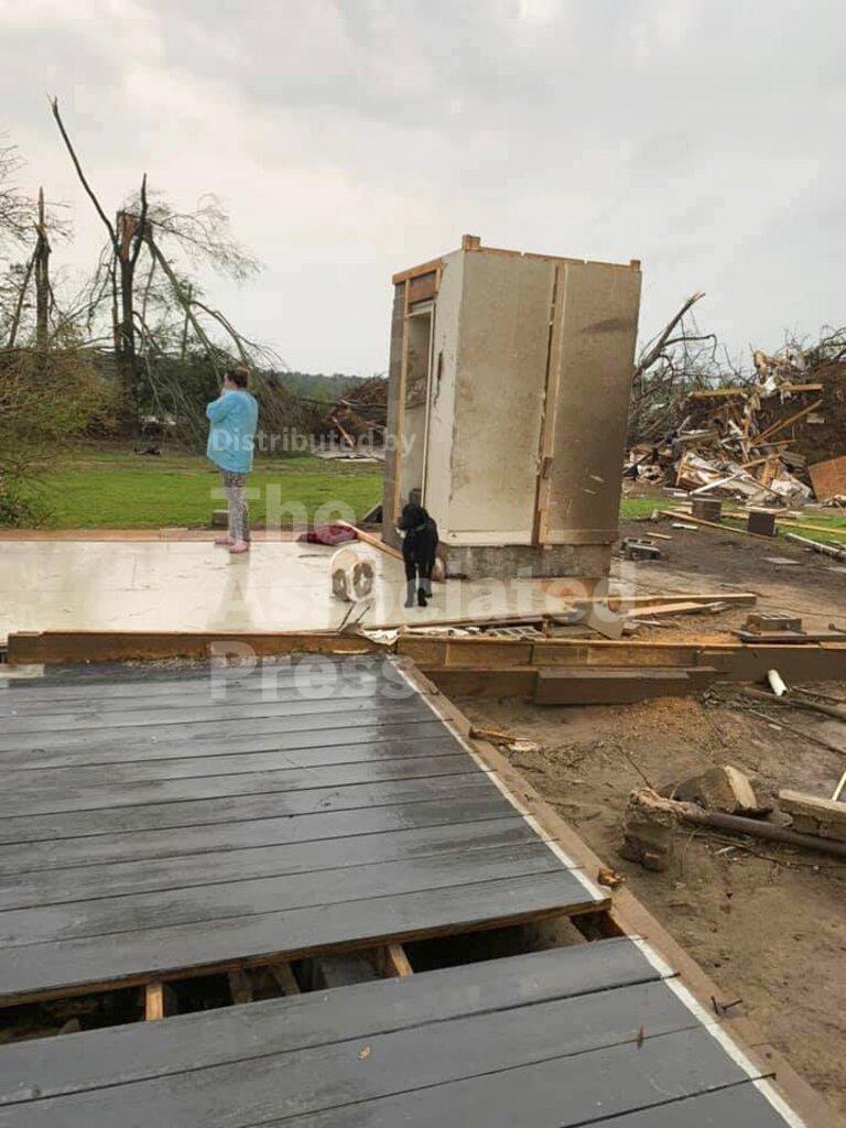 Amber Phillips stands outside the family's safe room, located on their property in Moss, Miss., following a tornado, Monday, April 13, 2020. While the rest of their home was obliterated in a matter of seconds Sunday afternoon, Andrew Phillips, his wife Amber and their kids, ages 2 and 6 months, survived the storm without a scratch inside the small safe room, which doubles as a closet. (Andrew Phillips via AP)