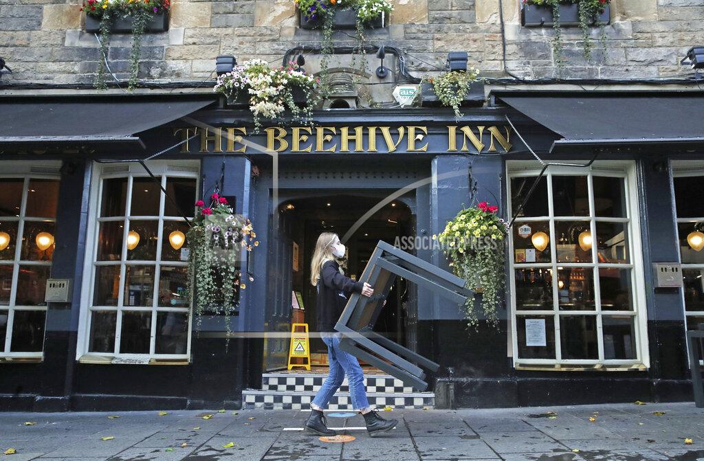 A worker removes tables from outside the Beehive Inn, as temporary restrictions announced by First Minister Nicola Sturgeon to help curb the spread of coronavirus have come into effect from 6pm, in Edinburgh, Friday, Oct. 9, 2020. (Andrew Milligan/PA via AP)