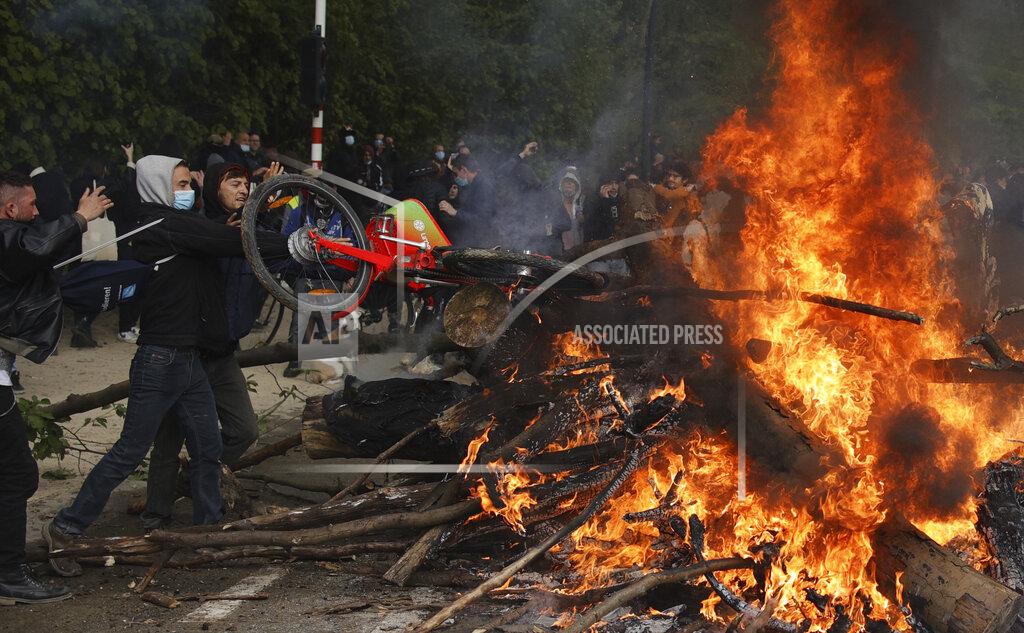 Olivier Matthys Two men throw a bicycle onto a bonfire at the Bois de la Cambre park during a party called "La Boum 2" in Brussels, Saturday, May 1, 2021. A few thousand people gathered for an illegal party in a Brussels park Saturday to protest COVID-19 restrictions, only to be met with a big police force who used a water cannon and tear gas to disperse the crowd. It was the second such open-air gathering in a month. (AP Photo/Olivier Matthys)